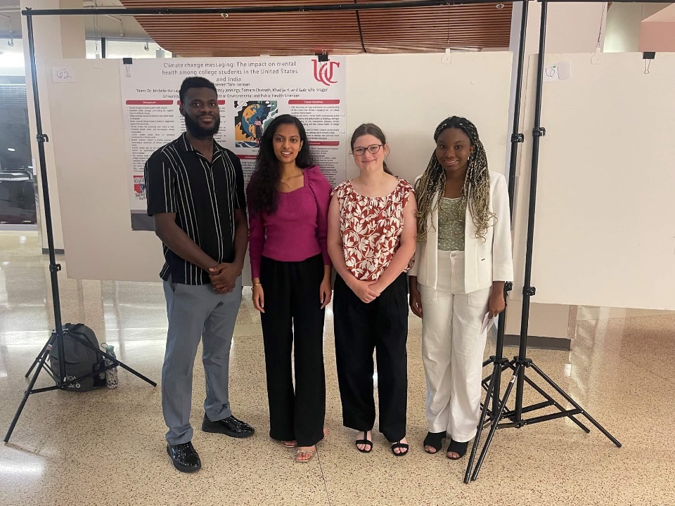 four people standing in front of a poster presentation board