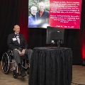 A man in a wheelchair giving a speech with a slideshow