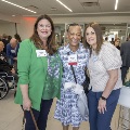 Three women post with many others mingling in the background