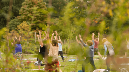 a large group of people with their hands in the air performing yoga in the park