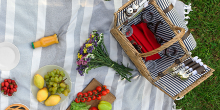 a picnic blanket placed on grass and basket with a bouquet of flowers and fresh fruit