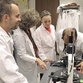 Man looking into microscope with 3 other looking on