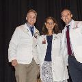 Three people wearing white coats pose for a photo